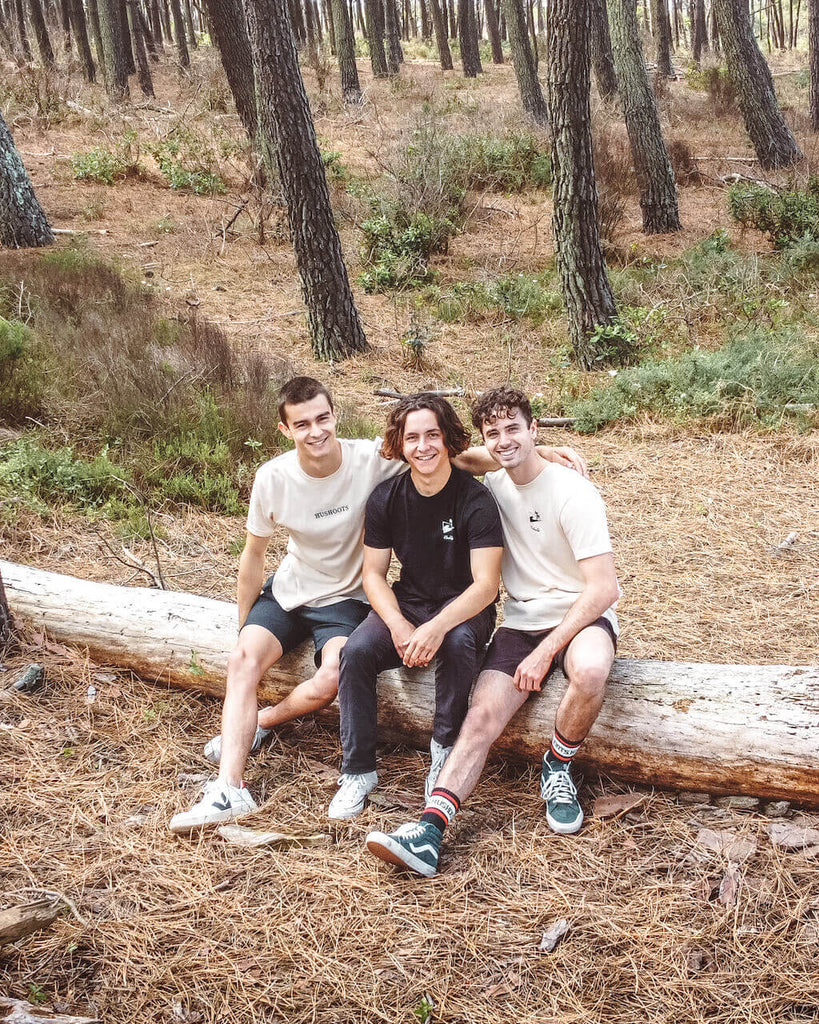 trois hommes assis sur un tronc d'arbre en t-shirt